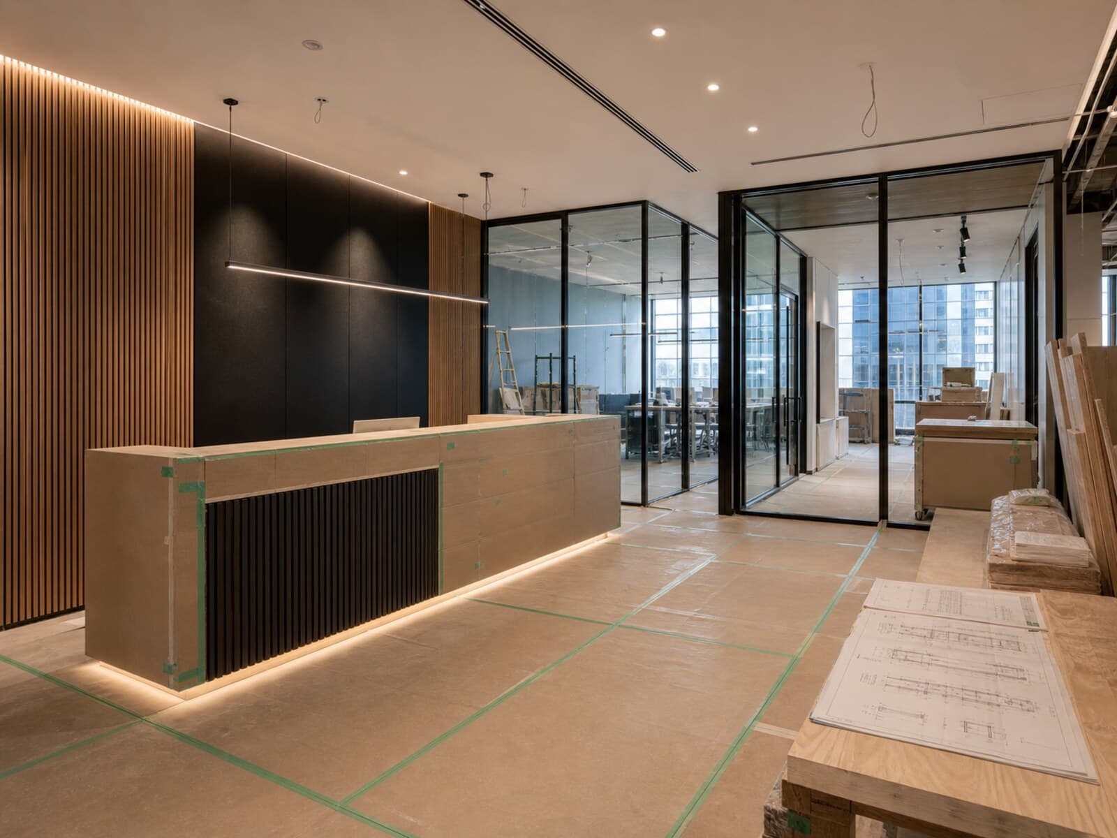 Commercial office fitout in progress with a reception area, glass meeting room, construction materials, and exposed ceiling services.